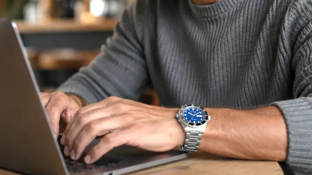 Man typing on a laptop wearing a stainless steel automatic sports watch