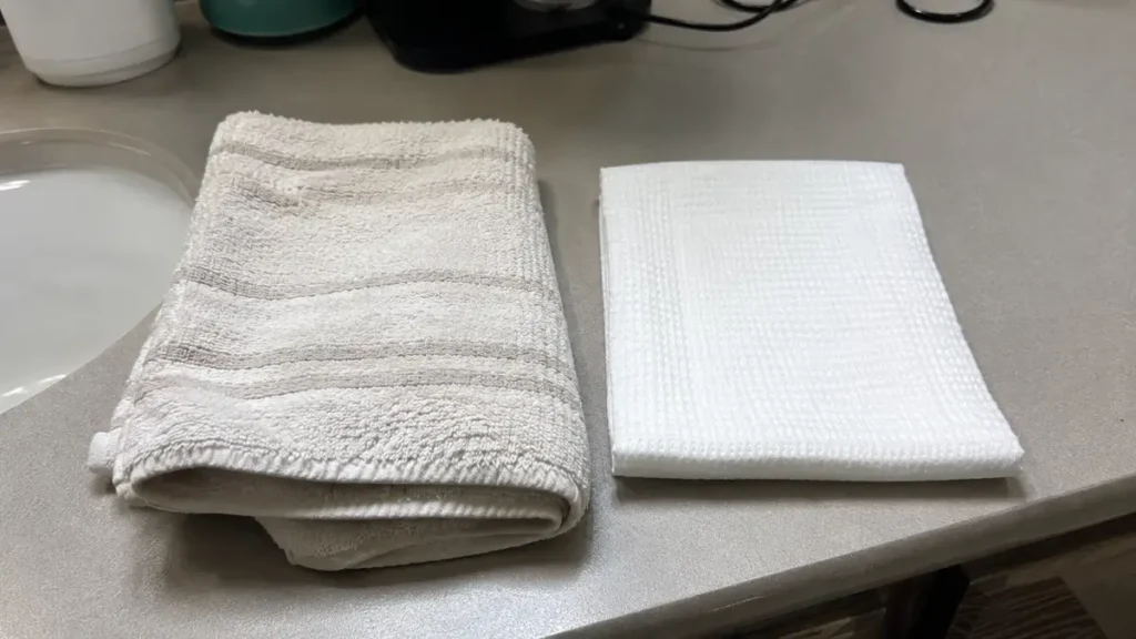A reusable cotton towel beside a single-use facial towel on a bathroom counter