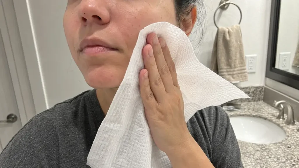 A woman gently pressing a disposable facial towel against her cheek after cleansing