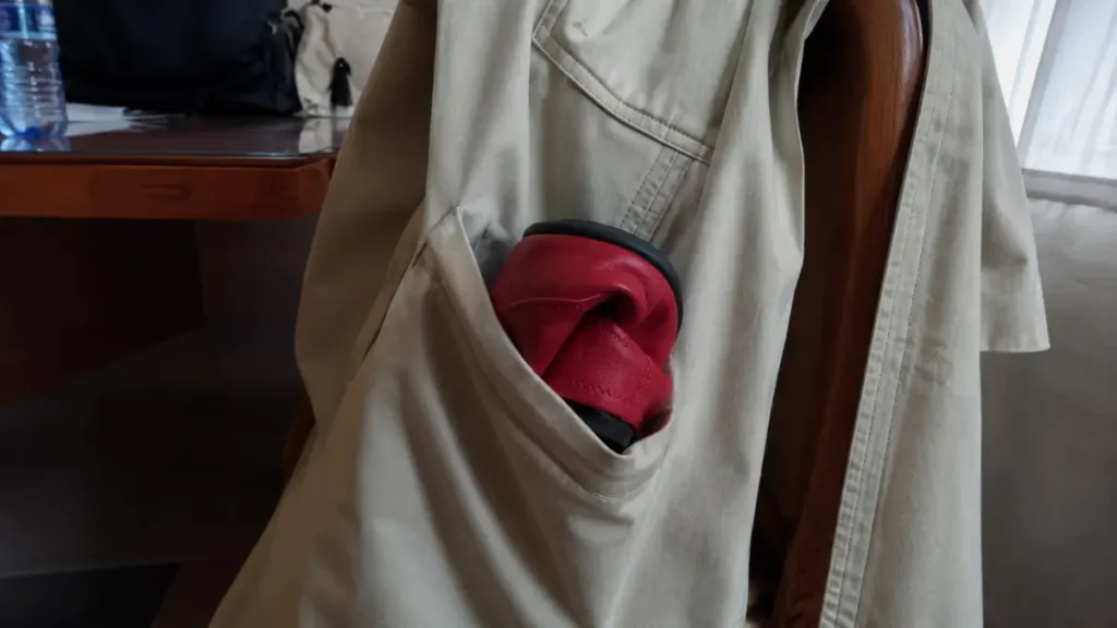 Bright red flat shoes folded and tucked into the pocket of a coat hanging on a chair.