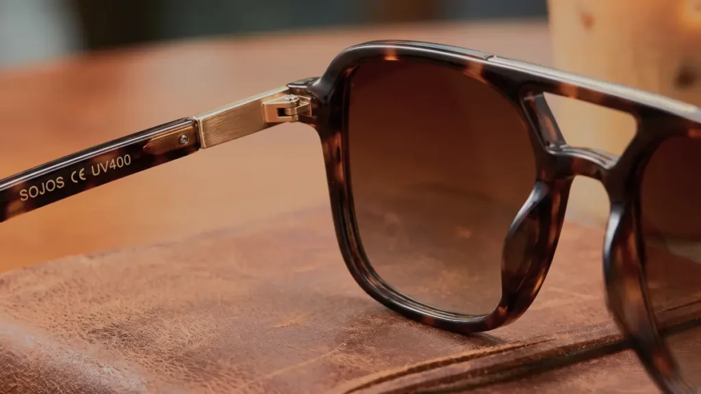 A hand holding tortoise shell sunglasses above an open leather handbag.