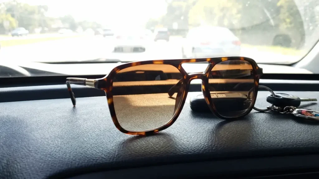 Rectangular tortoise shell sunglasses placed on a car dashboard with bright sunlight in the background.