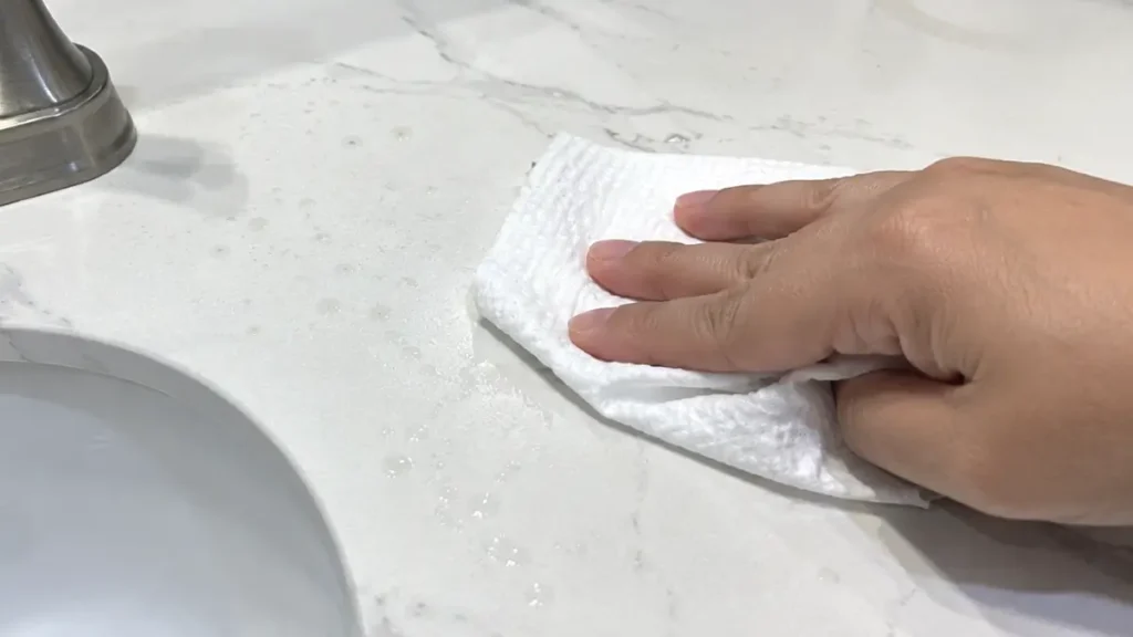 A used facial towel wiping water spots from a bathroom faucet area