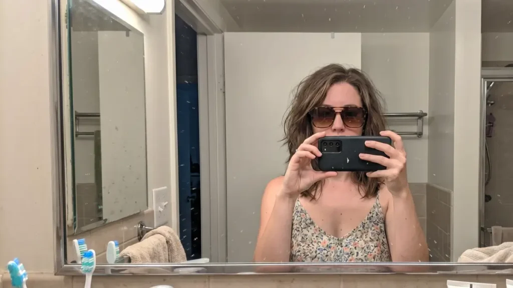 A woman taking a mirror selfie wearing tortoise shell aviators and a summer dress.