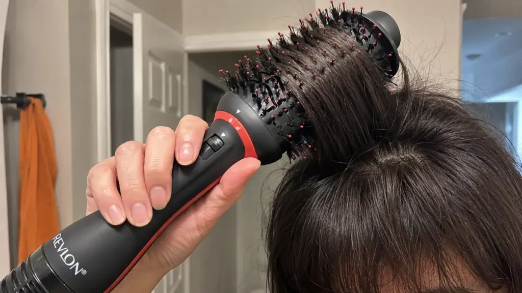 A woman's hands using the slim handle of a blow dryer brush to style thick hair.
